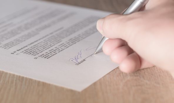 Gedruckter Vertrag, der gerade von jemandem mit einem Kugelschreiber unterschrieben wird. 