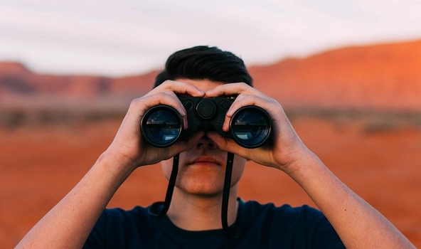 Ein Mann steht in einer Wüste und schaut durch ein Fernglas.