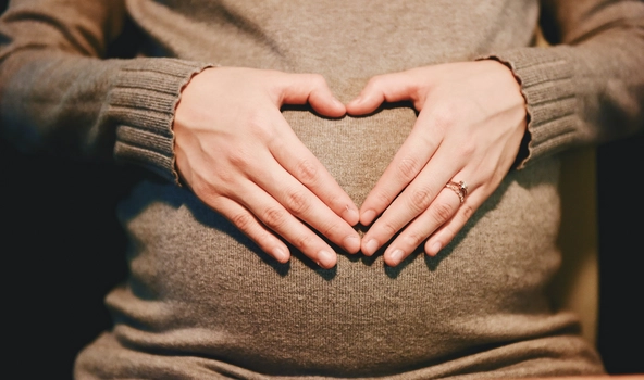 Bauch einer schwangeren Frau. Sie hat ihre Hände auf den Bauch gelegt, sodass die Form eines Herzes entsteht.