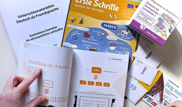 Auf einem Tisch liegen verschiedene Hefte zum Lernen. Eine Hand zeigt auf eines davon.