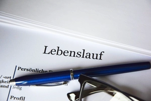 Oberer Teil eines gedruckten Lebenslaufs. Darauf befindet sich ein blauer Kugelschreiber und eine schwarze Brille.