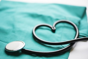 Stethoskop liegt auf grüner Klinik-Bekleidung. Der Schlauch ist als Herz geformt.