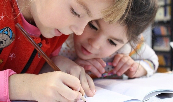 Zwei kleine Kinder beugen sich interessiert über ein Heft. Eines der Kinder schreibt etwas in das Heft hinein.